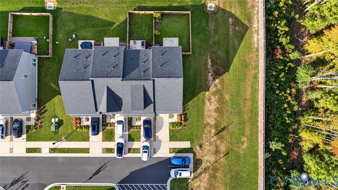 Aerial perspective featuring a multi-unit structure with dark shingle roofing, concrete driveways, individual fenced-in backyard areas, and perimeter woodland buffering