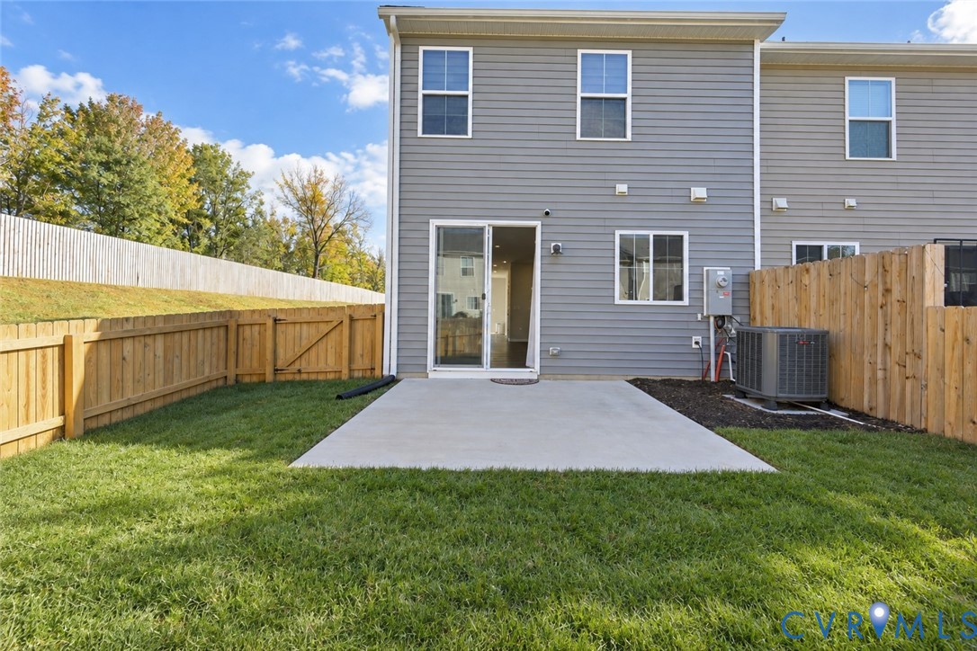 Rear exterior featuring gray horizontal siding, a concrete patio, a fenced yard, and a sliding glass door