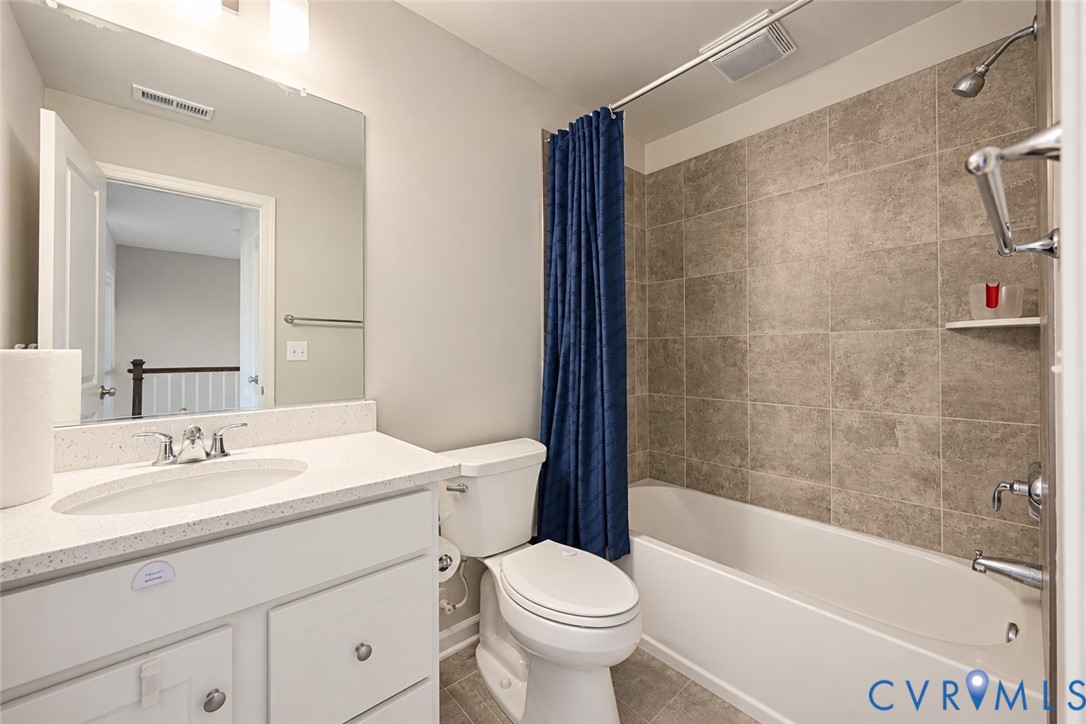 Bathroom featuring a vanity with a light-toned solid surface countertop and undermount sink, ceramic tile shower surround, and a large wall-mounted mirror