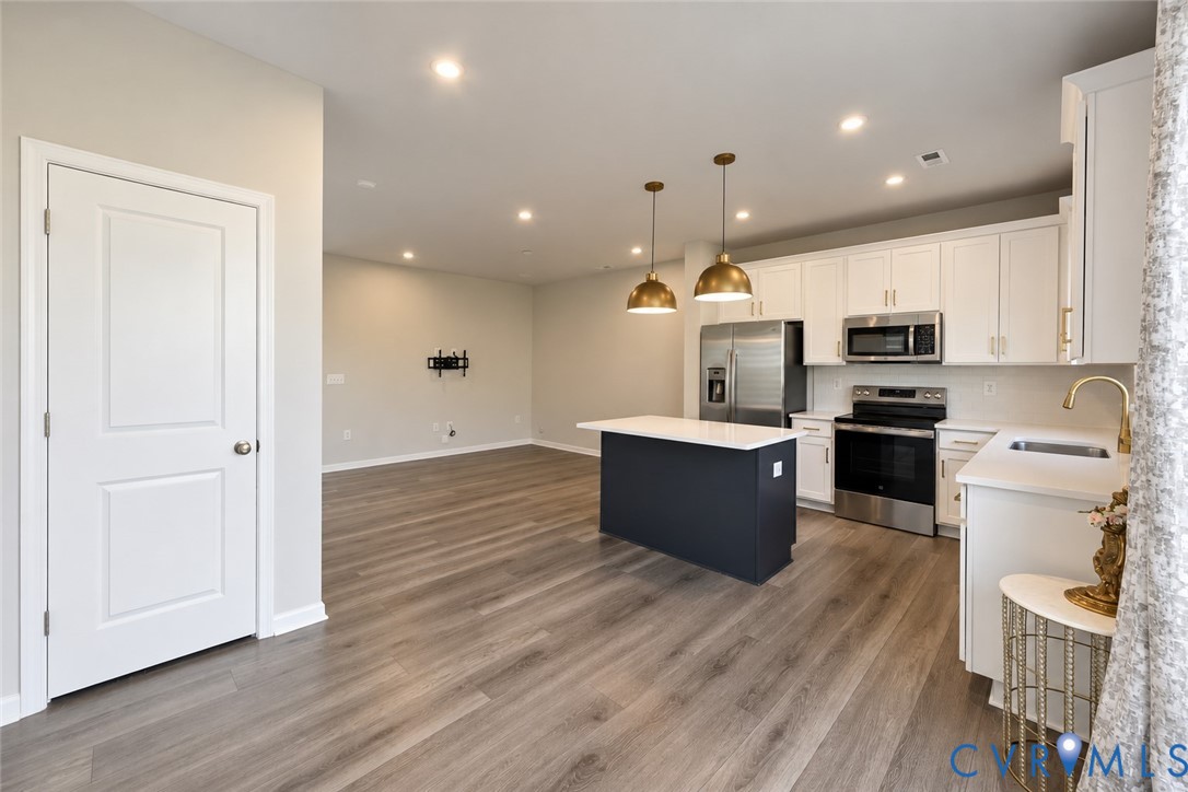 Kitchen featuring white cabinetry, quartz countertops, a dark-toned center island, stainless steel appliances, and wood-finish flooring