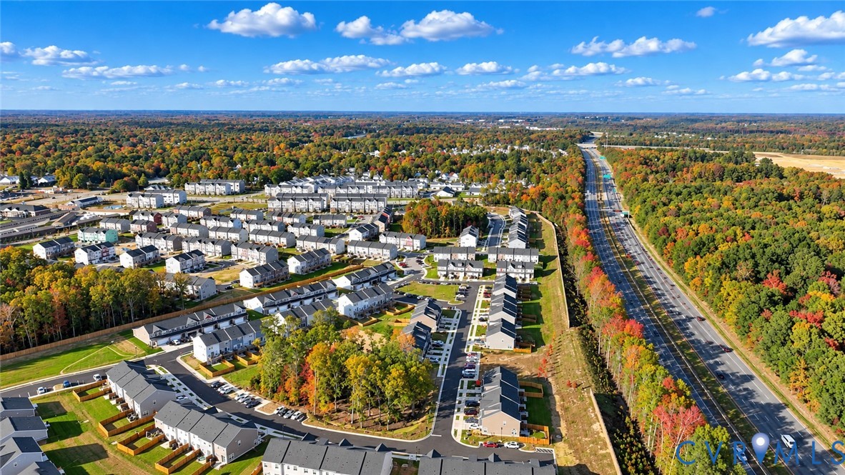 Aerial perspective of a multi-unit residential community featuring asphalt roadways, perimeter greenery, paved parking surfaces, and proximity to regional infrastructure