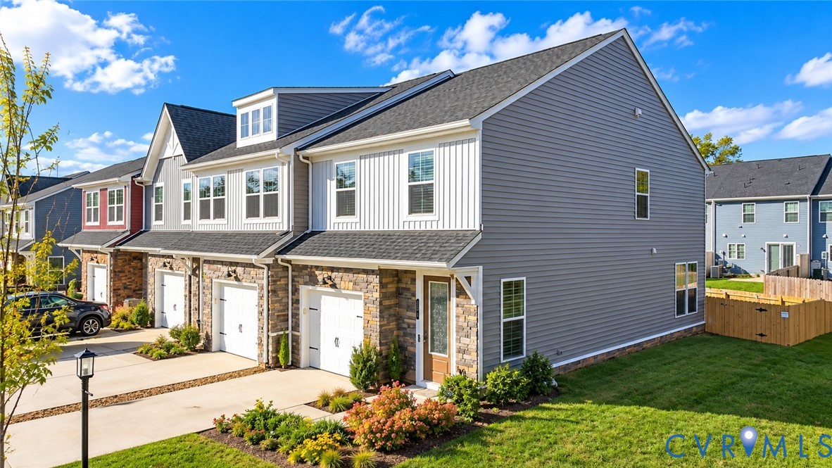 Multi-level townhouse featuring a mixed-material facade of stone veneer and horizontal siding, an attached garage, and a gable roof with dormer windows Multi-level townhouse featuring a mixed-material facade of stone veneer and horizontal siding, an attached garage, and a gable roof with dormer windows