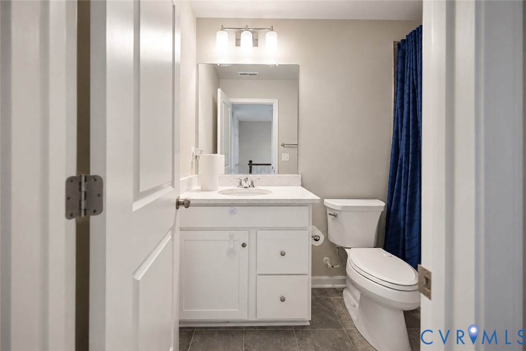 Bathroom featuring a white vanity with stone-composite countertop, undermount sink, three-light fixture, and stone-finish tile flooring