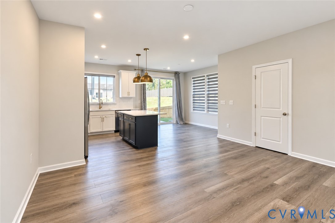 Kitchen featuring wood-finish flooring, a center island with a stone countertop, dual metal pendant lighting, and white cabinetry