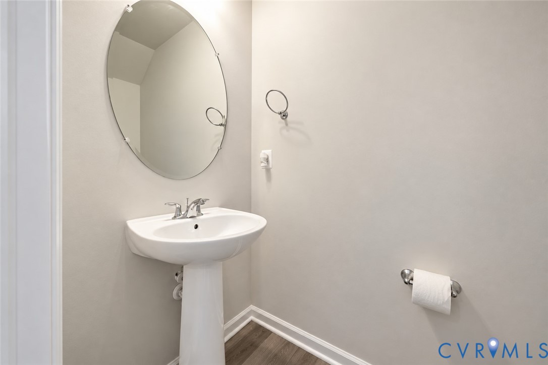 White pedestal sink with chrome faucet, oval frameless mirror, and wood-finish flooring