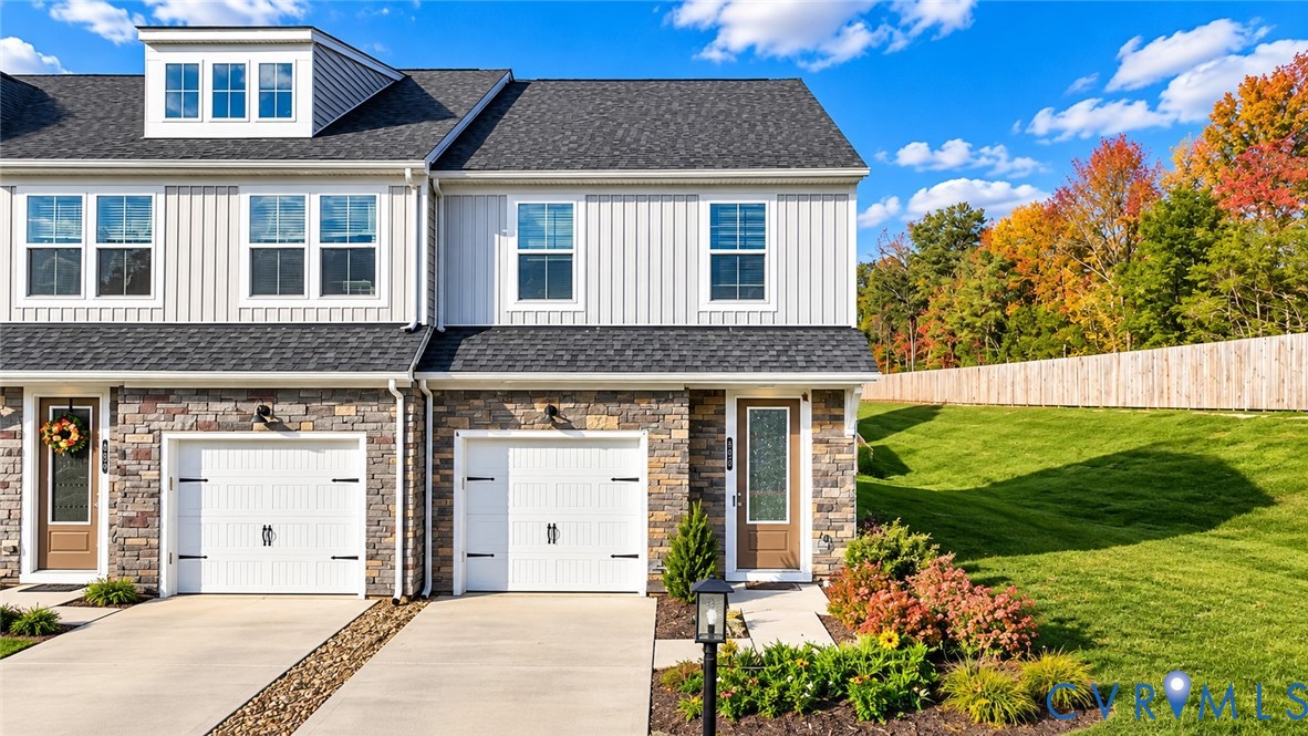 Townhome exterior featuring stone masonry, board-and-batten siding, a dormer window, dual-car garages, and an expansive grass lawn