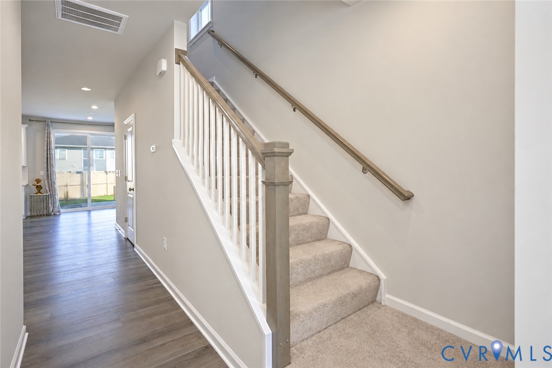 Staircase featuring white balusters, wood-finish handrail, and carpeted treads, complemented by wood-finish flooring and recessed lighting