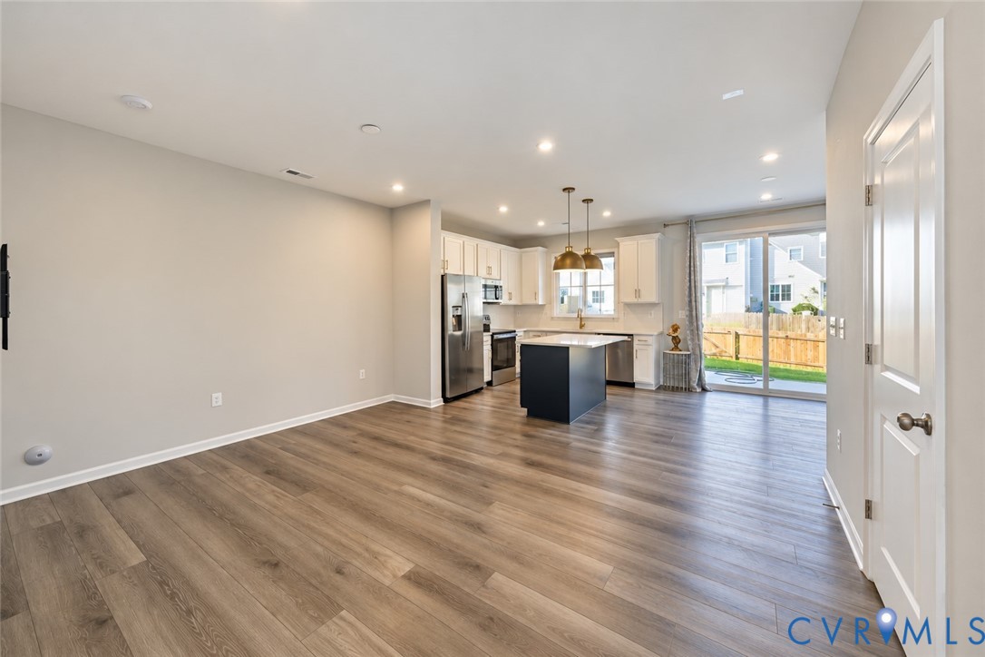 Kitchen featuring white cabinetry, a center island with a dark base, stainless steel appliances, recessed lighting, and wood-finish flooring Kitchen featuring white cabinetry, a center island with a dark base, stainless steel appliances, recessed lighting, and wood-finish flooring