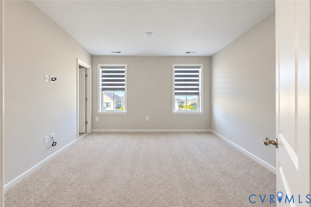 Neutral-toned room featuring plush wall-to-wall carpeting, dual windows with integrated shades, and a six-panel door