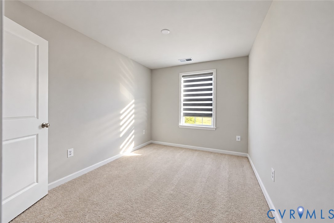 Interior room featuring neutral-toned carpeting, light-colored walls, a single-panel interior door, and a window equipped with striped roller shades