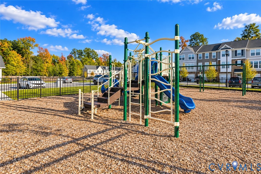 Community playground featuring a multi-level structure with a slide, climbing bars, stairs, and a wood-mulch surface enclosed by perimeter fencing