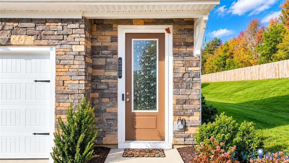 Exterior facade featuring stacked stone veneer, white garage door with decorative hardware, and a solid-panel entry door with a vertical glass insert Exterior facade featuring stacked stone veneer, white garage door with decorative hardware, and a solid-panel entry door with a vertical glass insert
