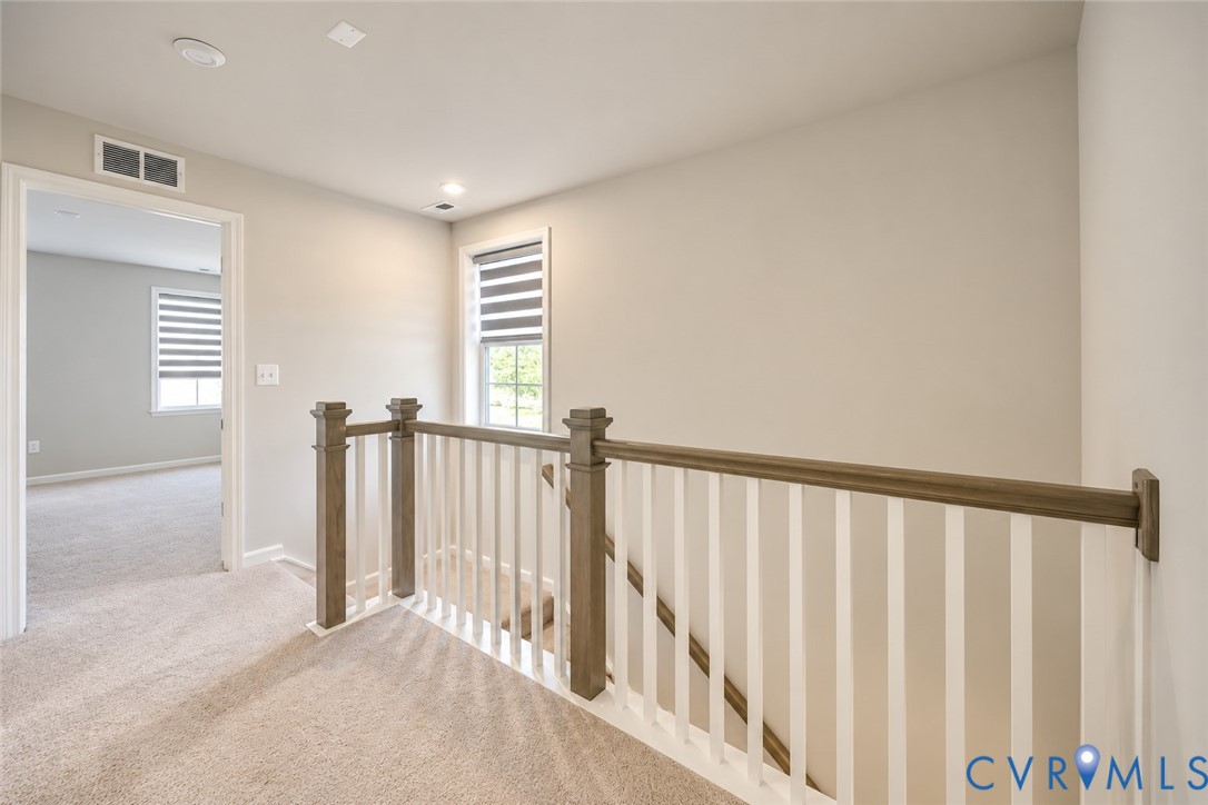 Neutral-toned carpeting, wood-finish handrail, white vertical balusters, and dual-layered window blinds