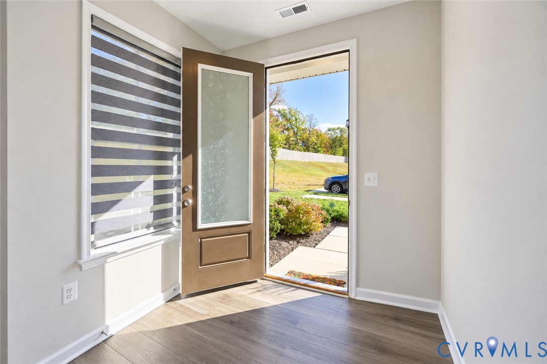 Entryway featuring wood-finish flooring, a solid-core front door with an integrated frosted glass panel, and a multi-banded roller shade Entryway featuring wood-finish flooring, a solid-core front door with an integrated frosted glass panel, and a multi-banded roller shade