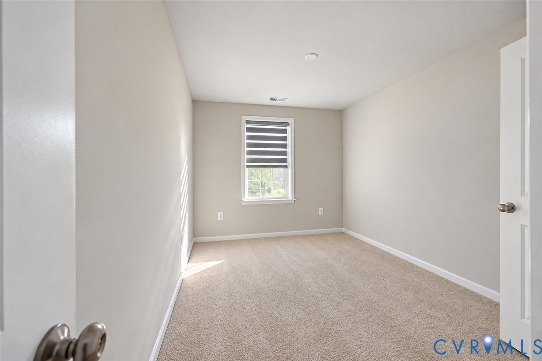 Neutral-toned interior space featuring wall-to-wall carpeting and a single window equipped with an integrated dual-shade blind