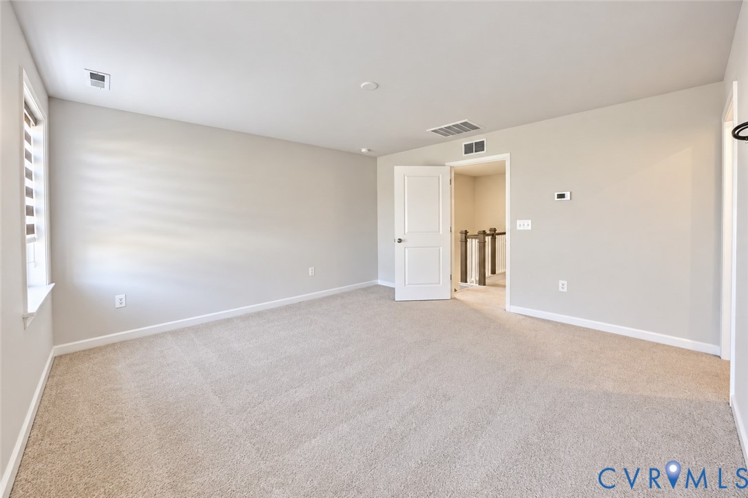 Neutral-toned interior space featuring wall-to-wall carpeting, a multi-panel interior door, and window treatments with horizontal blinds