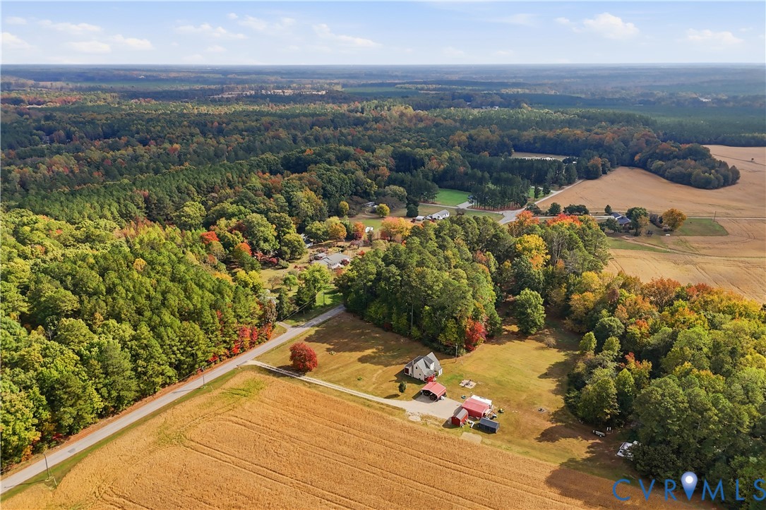 Aerial perspective featuring expansive acreage, open fields, forested boundaries, and multiple outbuildings