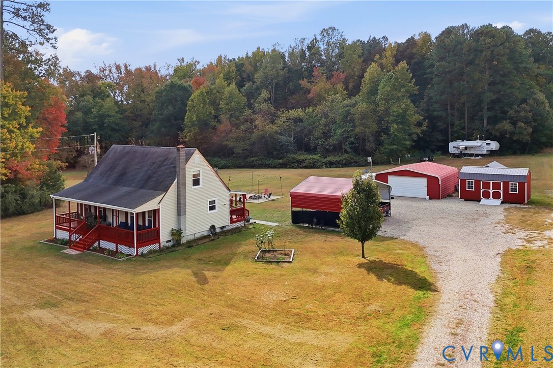 Expansive lot featuring a residence with a covered porch, detached garage, storage shed, and metal-roofed carport