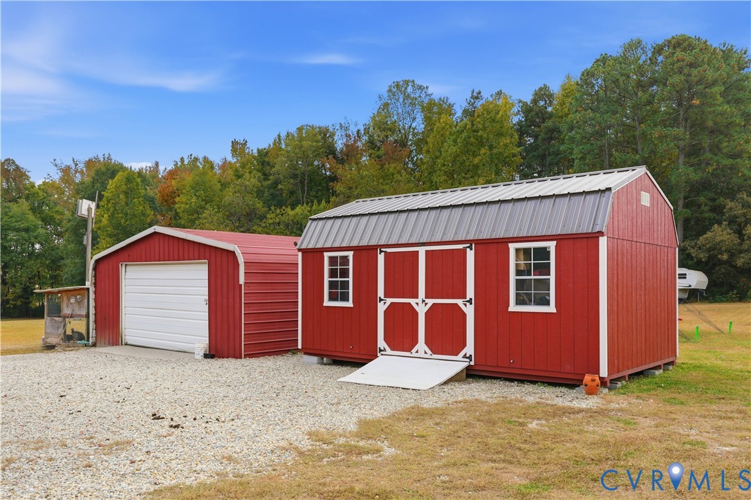Detached metal storage structure and separate one-car garage featuring gravel drive access