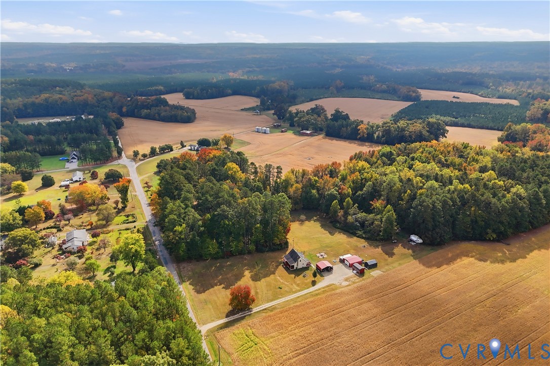 Aerial perspective of expansive acreage featuring large tracts of open pasture, mature forested areas, a primary structure, and multiple outbuildings