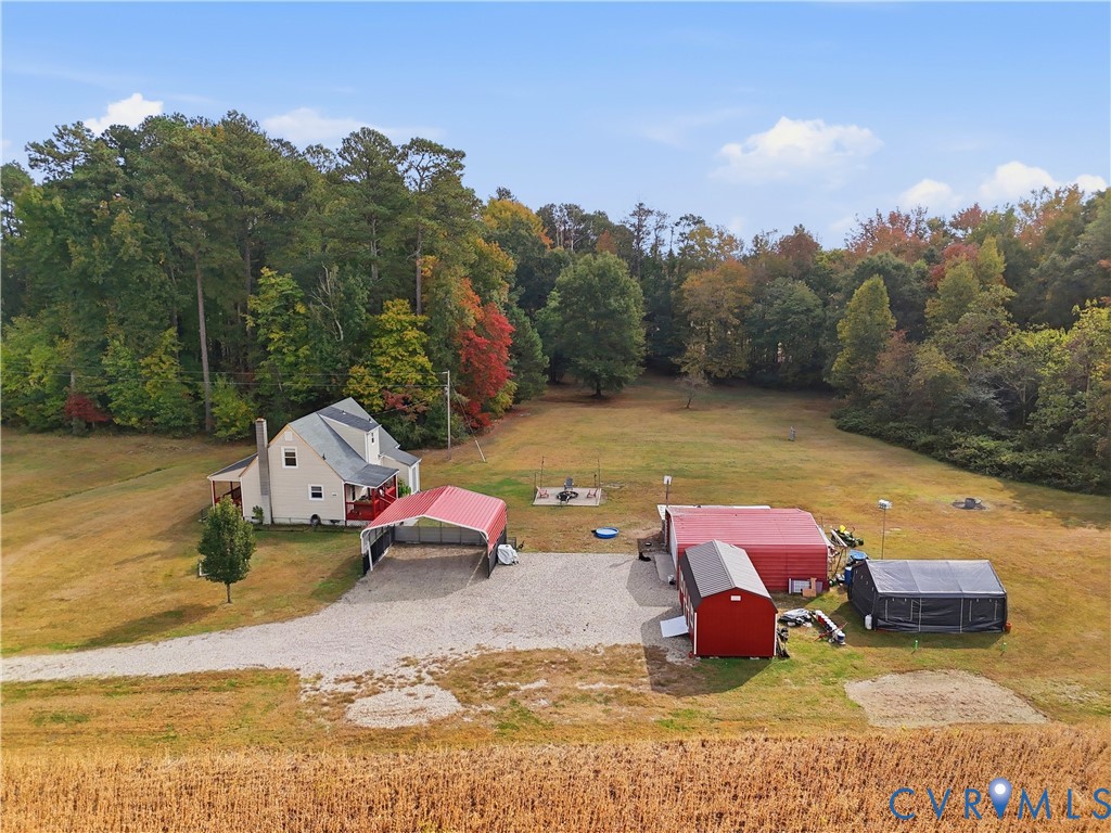 Expansive lot featuring mature perimeter trees, a detached multi-bay metal structure, a gravel driveway, and a residential building with a covered exterior entry