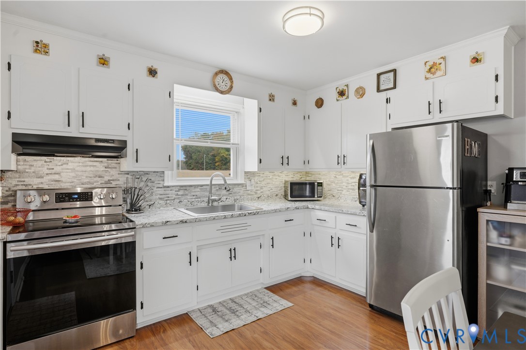 Kitchen featuring white cabinetry, stone-finish countertops, stainless steel appliances, multi-tonal tile backsplash, and wood-finish flooring