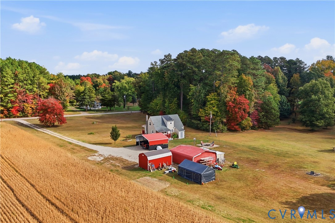 Extensive acreage featuring multiple outbuildings, metal-roofed storage structures, a gravel driveway, and mature perimeter trees