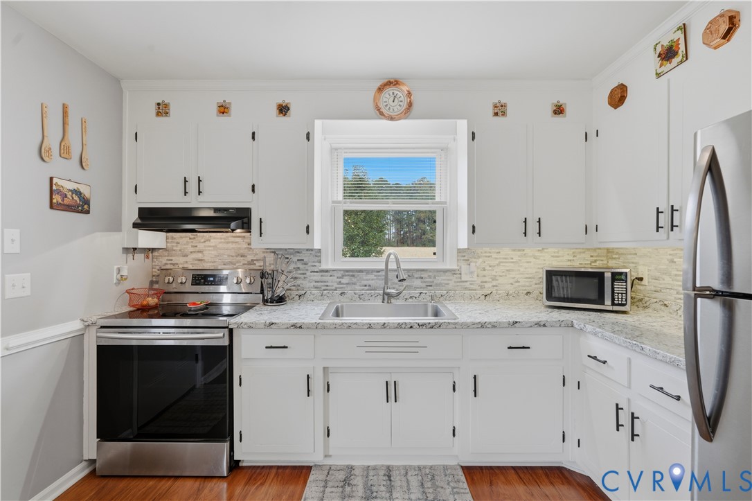 Kitchen featuring white cabinetry, stone-finish countertops, decorative tile backsplash, stainless steel sink, and wood-finish flooring