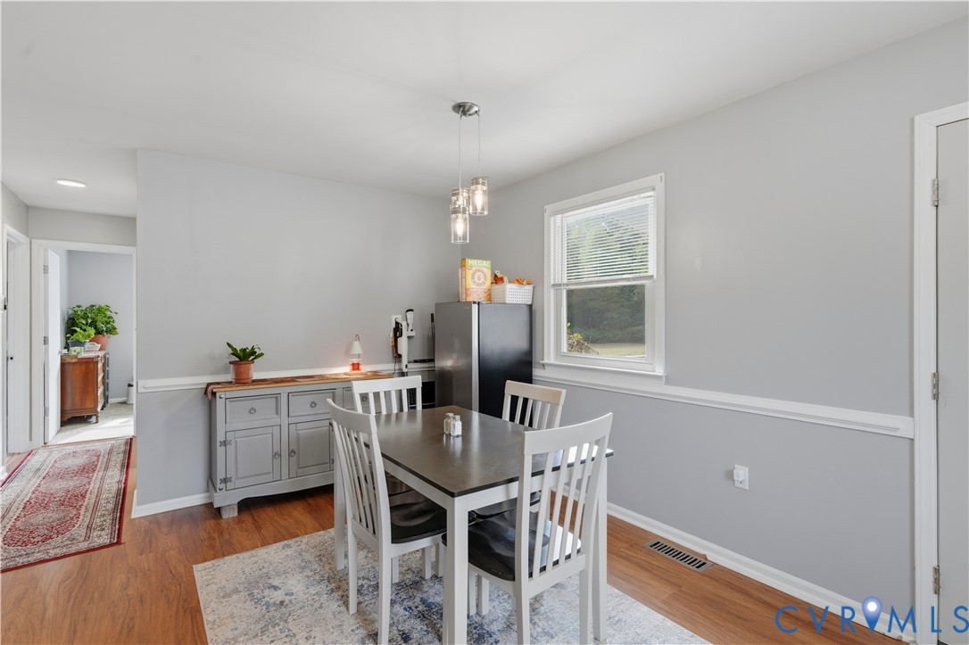 Dining area featuring wood-finish flooring, chair rail molding, and three-light glass pendant fixture