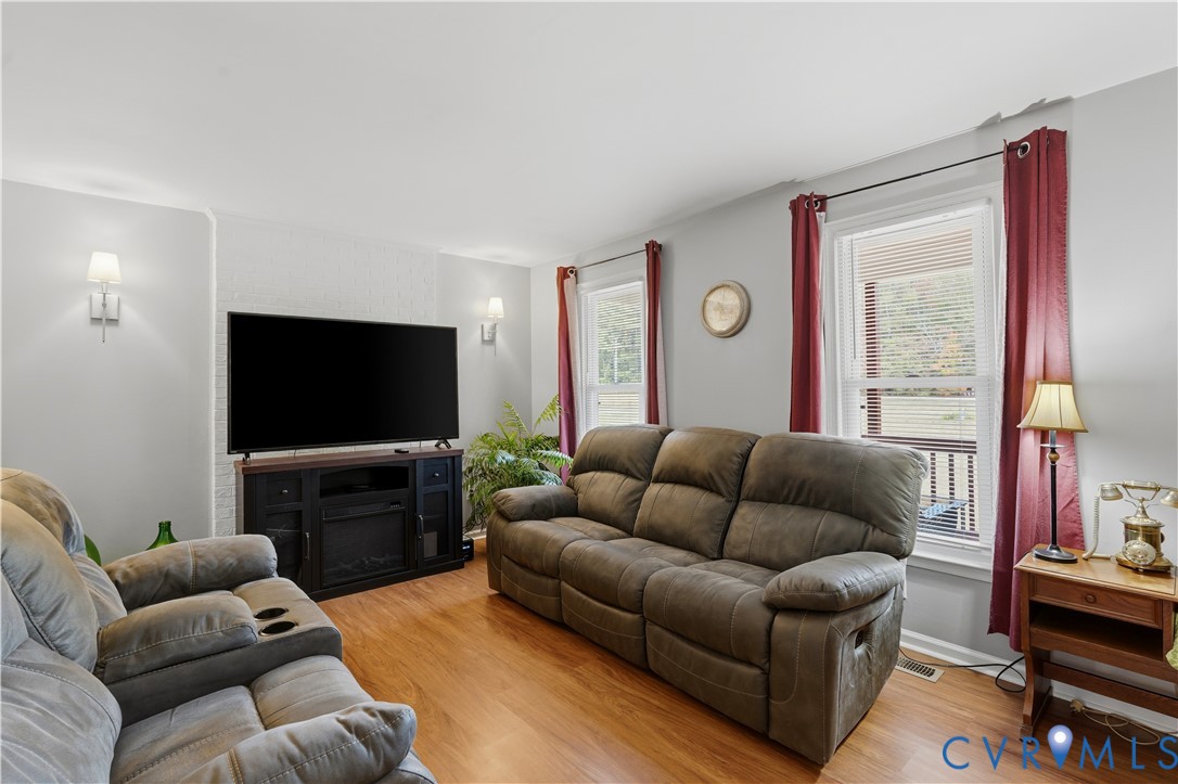 Living area featuring wood-finish flooring, white painted brick accent wall, and dual wall-mounted light fixtures