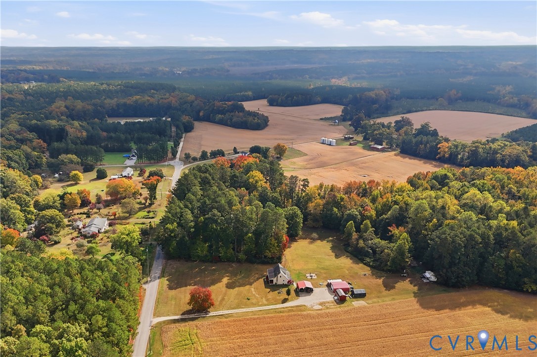 Aerial perspective of expansive acreage featuring mature woodland, open pastures, multiple outbuildings, and paved road access