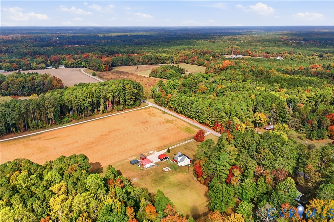 Aerial perspective of a multi-acre property featuring open pasture land, multiple outbuildings, and extensive surrounding woodland