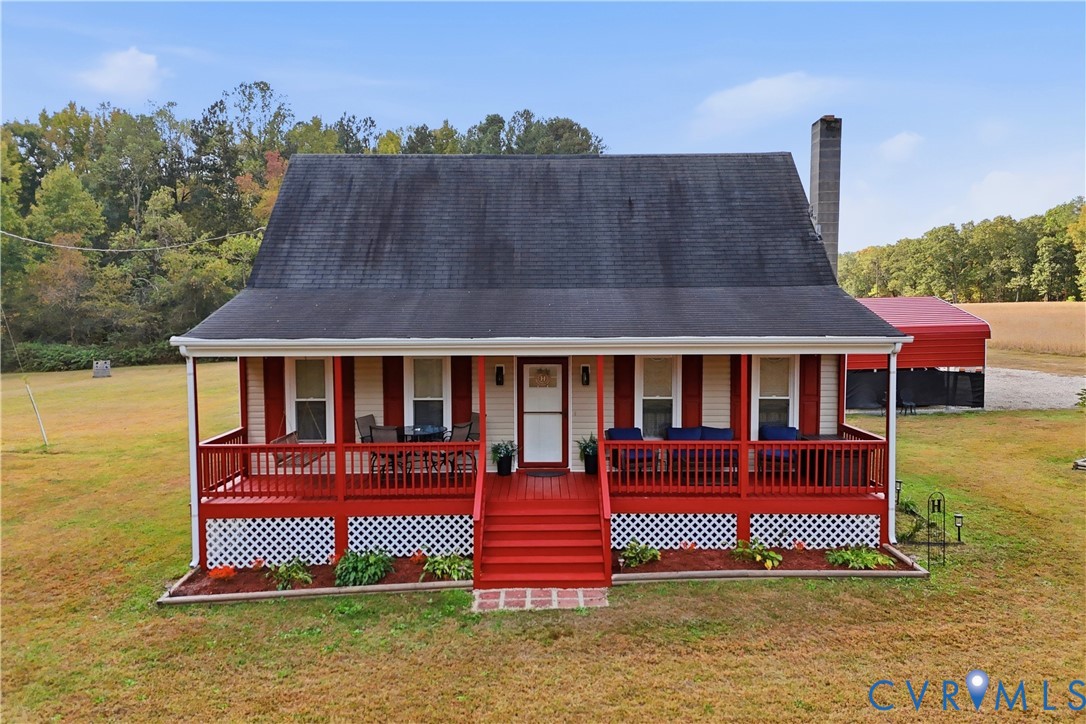 Single-story residence featuring a full-width covered front porch, red wood railings, decorative lattice skirting, exterior masonry chimney, and metal-roofed detached structure