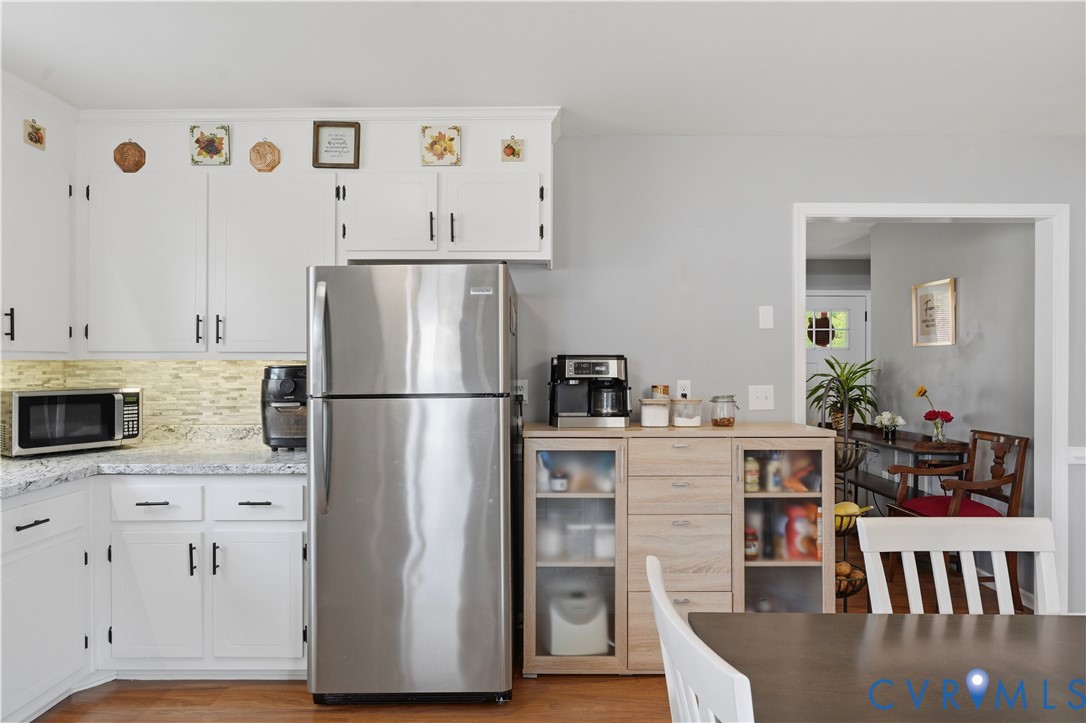 Kitchen featuring white shaker-style cabinetry, light-toned stone-finish countertops, mosaic tile backsplash, stainless steel refrigerator, and wood-finish flooring