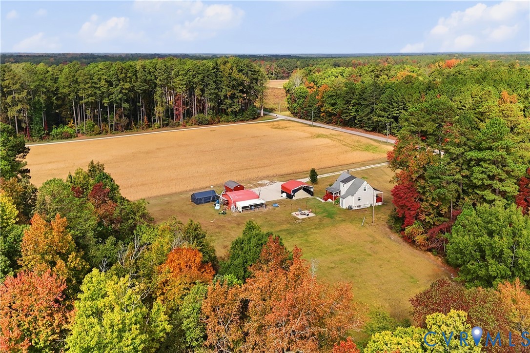 Expansive acreage featuring cleared fields, mature tree lines, residential dwelling, and multiple detached outbuildings