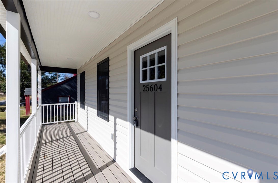 Covered front porch featuring white railing, horizontal vinyl siding, recessed ceiling lighting, and a six-panel front door with a glass inlay