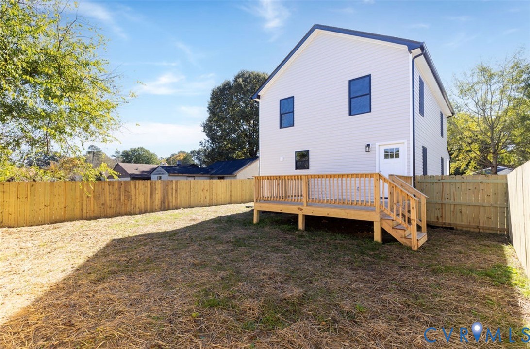 Two-story exterior with light-colored siding, elevated wood deck with stair access, and enclosed fenced backyard
