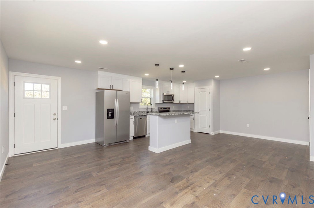 Kitchen featuring white shaker-style cabinetry, stone-surface countertops, stainless steel appliances, a center island with pendant lighting, and wood-finish flooring