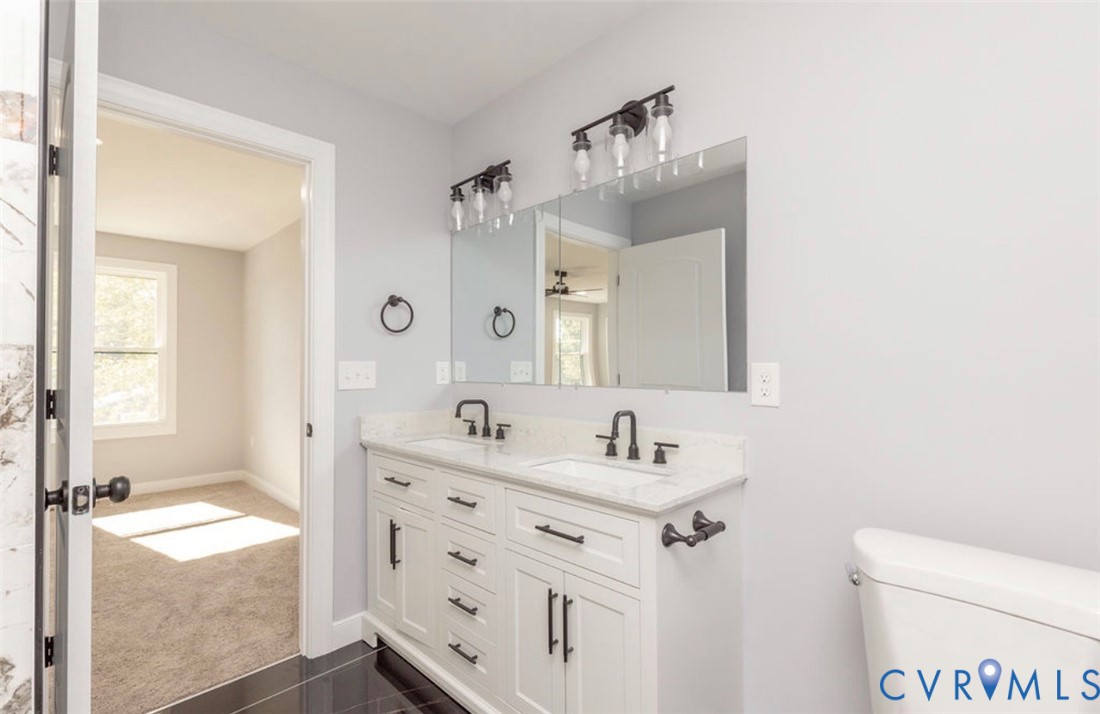 Double vanity featuring white cabinetry, stone-finish countertops, undermount sinks, matte black hardware, and wall-mounted lighting