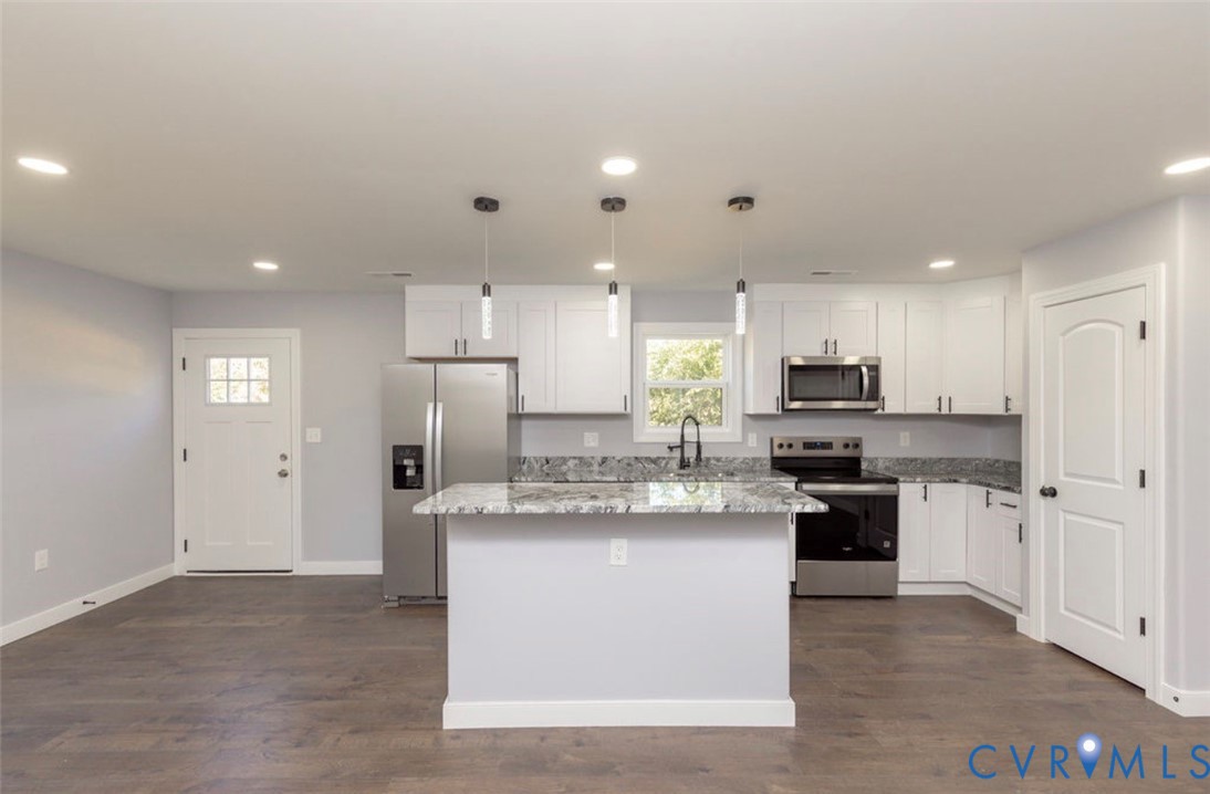 Kitchen featuring white shaker-style cabinetry, stone-surface countertops, wood-finish flooring, a central island, and stainless steel appliances