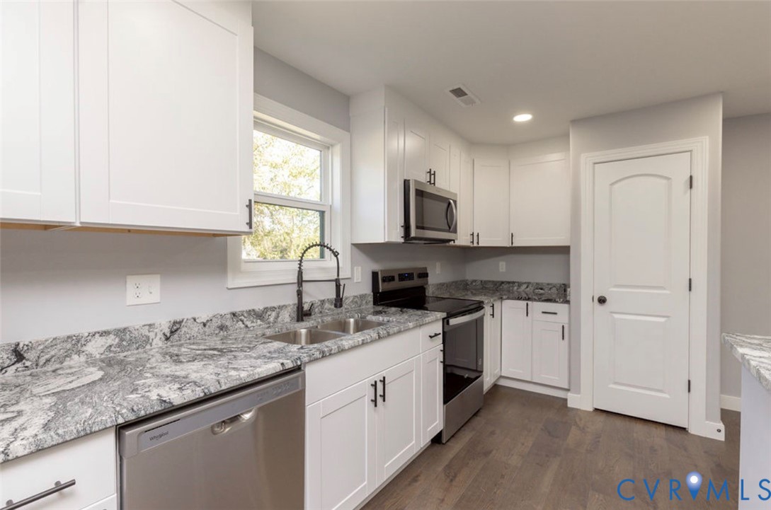 Kitchen featuring white shaker-style cabinetry, stone-patterned countertops, stainless steel appliances, a gooseneck faucet, and wood-finish flooring
