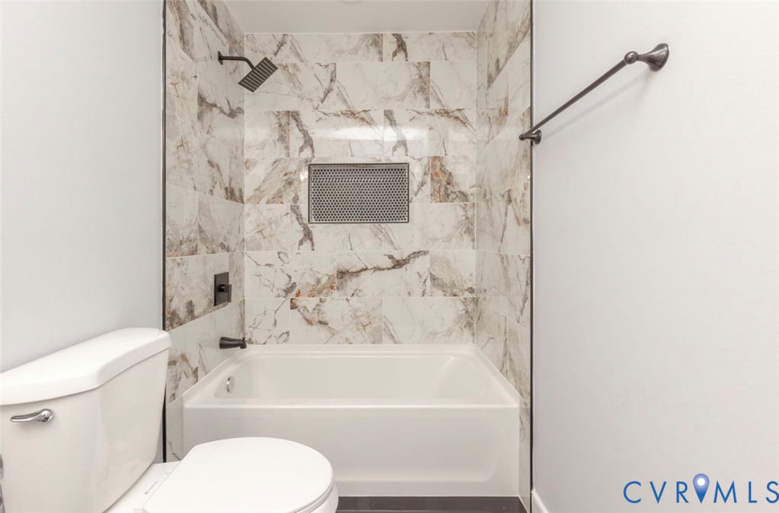Full-height tile surround with a marbled pattern, integrated shower niche, matte black rainfall showerhead, matte black hardware, and an alcove soaking tub