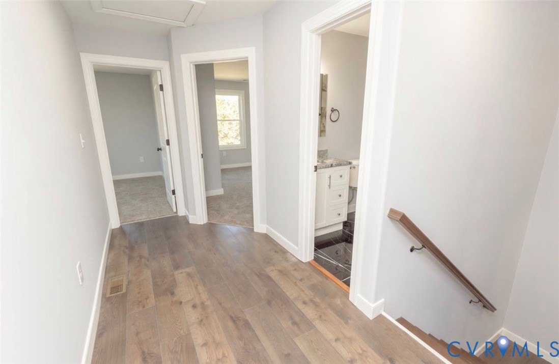 Hallway featuring wood-finish flooring, neutral wall tones, and a staircase with a wooden handrail