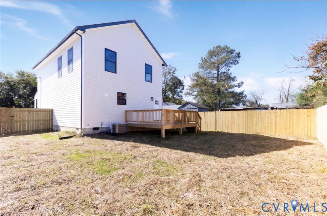 Rear exterior featuring light-toned horizontal siding, a wood deck, and a full-height privacy fence enclosing the yard