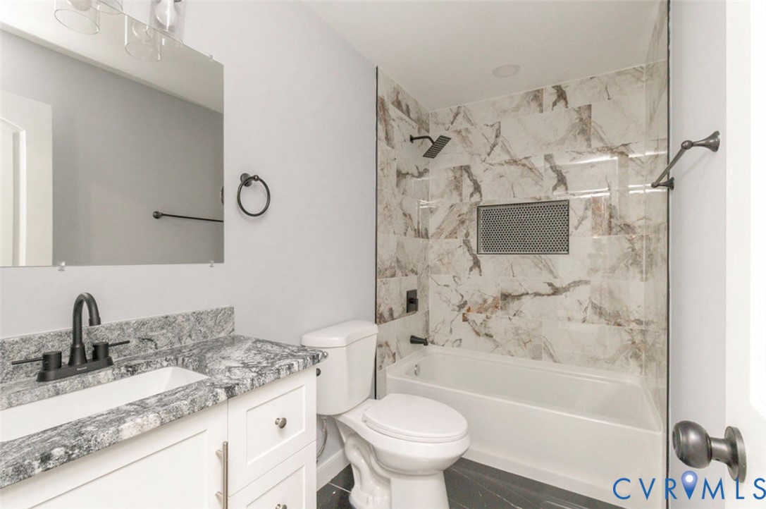 Bathroom featuring stone-patterned vanity countertop, white cabinetry, matte black hardware, and tub surround with decorative tile inlay