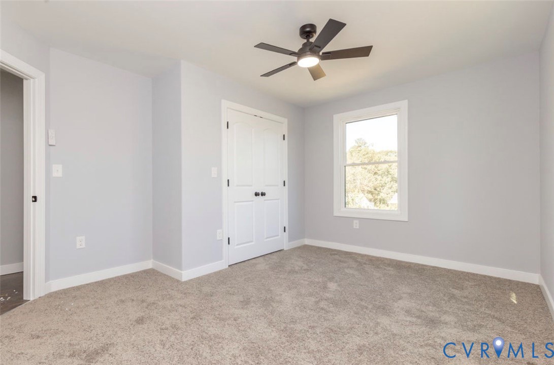 Neutral-toned wall paint, wall-to-wall carpeting, dual-door closet, multi-pane window, and integrated ceiling fan with lighting