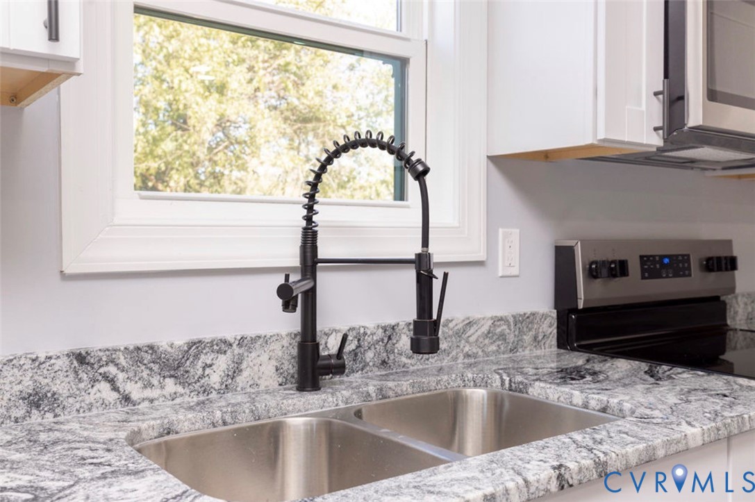 Dual-basin stainless steel sink featuring a matte black industrial-style pull-down faucet, stone-surfaced countertops with integrated backsplash, and crisp white cabinetry