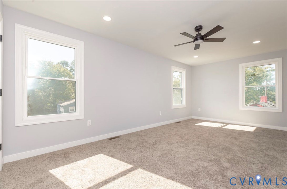 Neutral-toned interior room featuring wall-to-wall carpeting, recessed ceiling lighting, a dark-finish ceiling fan, and multi-pane windows