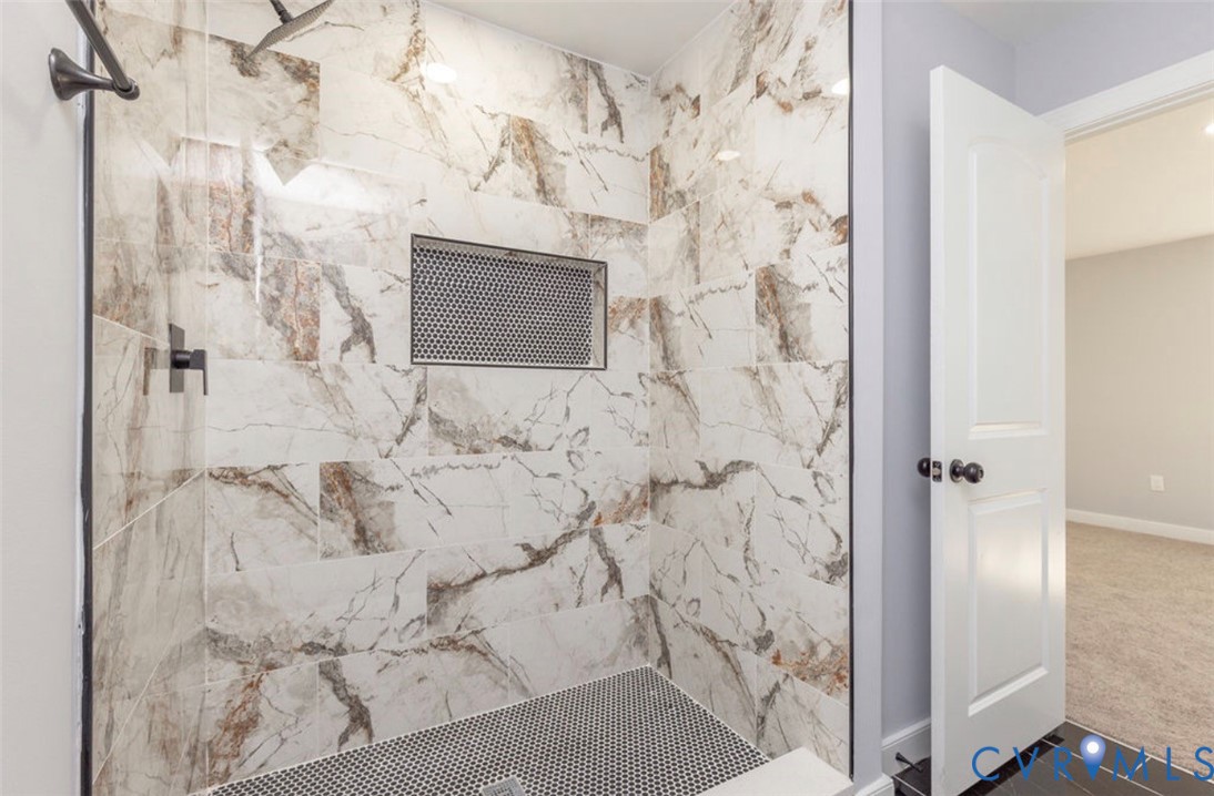 Walk-in shower featuring large-format patterned tile, mosaic-tiled floor, built-in tiled niche, and matte black plumbing fixtures