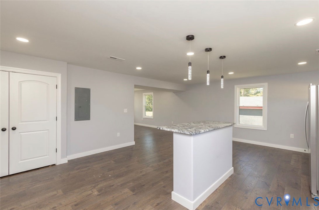 Kitchen island with stone-finish countertop, wood-finish flooring, recessed lighting, and three glass pendant lights